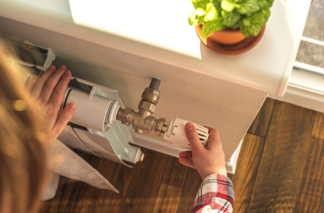 A person adjusts a radiator next to a windowsill with a green potted plant.