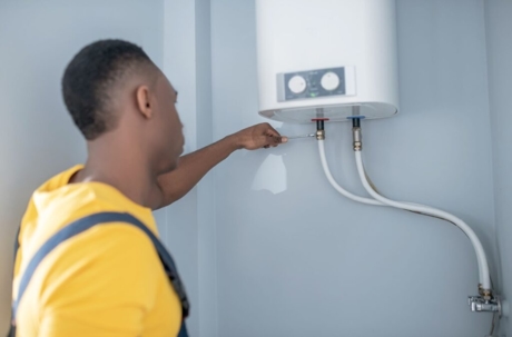A service provider is shown installing a tankless water heater on a light-colored wall.