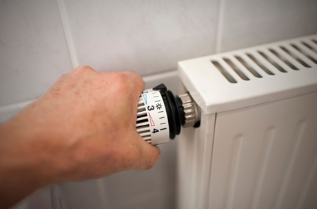 A thermostat is being adjusted on a white radiator.