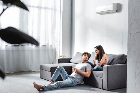 A modern living room with an air conditioner above a lounging couple.