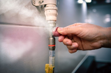 A hand twists the valve of a gas pipe, while gas escapes and condenses into visible white vapor.