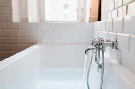 A white tub is being filled with water from a chrome faucet.