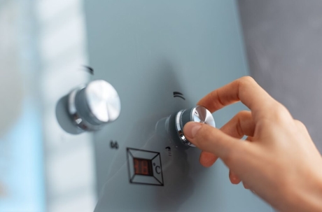 Close up of a hand turning a temperature dial on a tankless water heater.