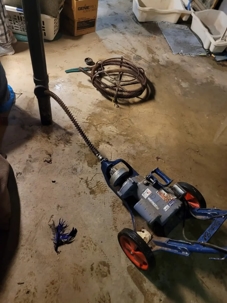 A motorized drain snake sits on a basement floor, ready to unclog a sewer line