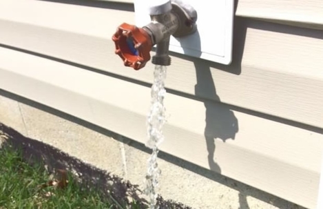 An exterior faucet with a red handle flows with water into the yard