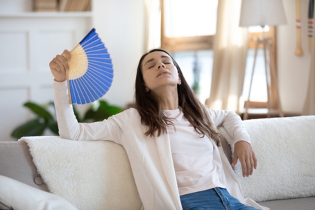 A woman sits on a couch, fanning herself