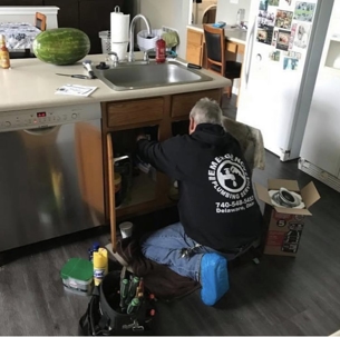 A plumber works under a kitchen sink, fixing plumbing