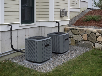 Two gray, square air conditioning units sit outside a house