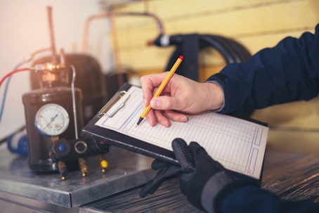 A worker wearing gloves takes notes on a clipboard while inspecting equipment