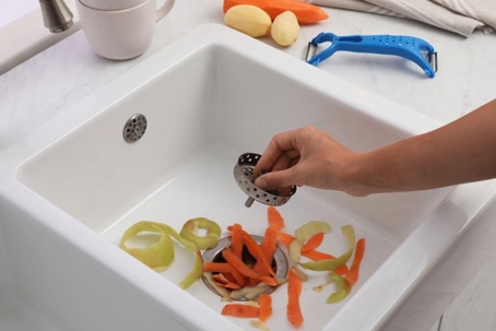 A person places a strainer in a white porcelain sink to prevent vegetable scraps from clogging the drain