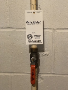 Main water shut-off valve on white pipe between cinder block wall