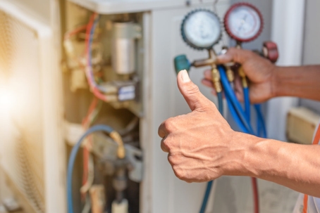 Close-up of a hand giving a thumbs up in front of an HVAC unit and gauges.