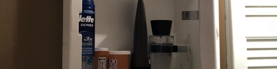 A partial view of a medicine cabinet, where razors, shaving cream, and medicine bottles are stored