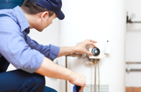 A worker in a blue uniform adjusts the gas supply to a hot water tank.