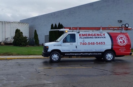 A branded work van sits roadside in front of a commercial building