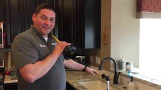 A man holds a plunger next to a kitchen sink, likely demonstrating plumbing tips.
