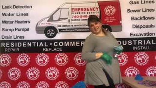 A woman stands smiling in front of an Emergency Plumbing Services backdrop.