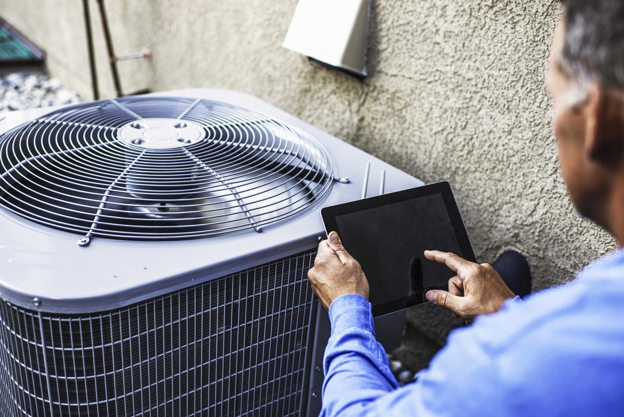 HVAC contractor using digital tablet to inspect air conditioning unit